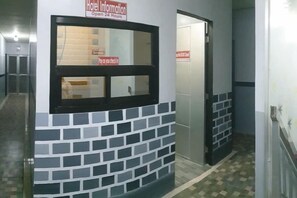 A hotel reception area with a check-in counter, a sign indicating 24-hour service, and a door leading to the hotel rooms.