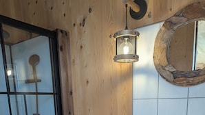 A bathroom with a wooden wall, a white toilet, a white sink with a black faucet, and a wooden-framed mirror. - Tiny house-style chalet with private spa on the Alsace border (Zilling)