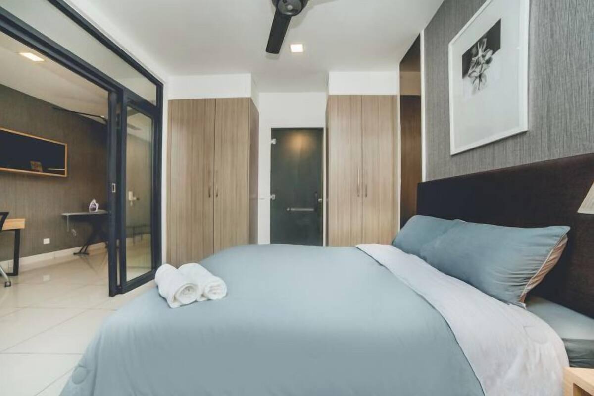A modern bedroom with a bed, a desk, and a door leading to another room.