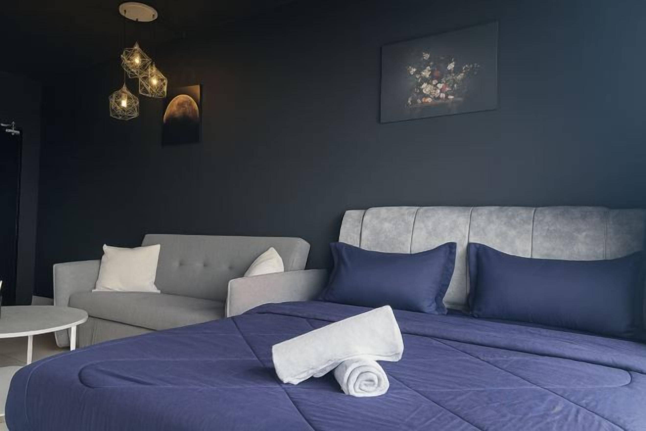 A modern hotel room with a large bed, a grey sofa, and a small round table.