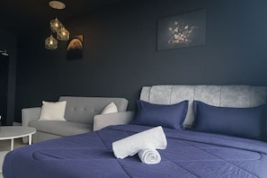 Ein modernes Hotelzimmer mit einem großen Bett, einem grauen Sofa und einem kleinen runden Tisch.