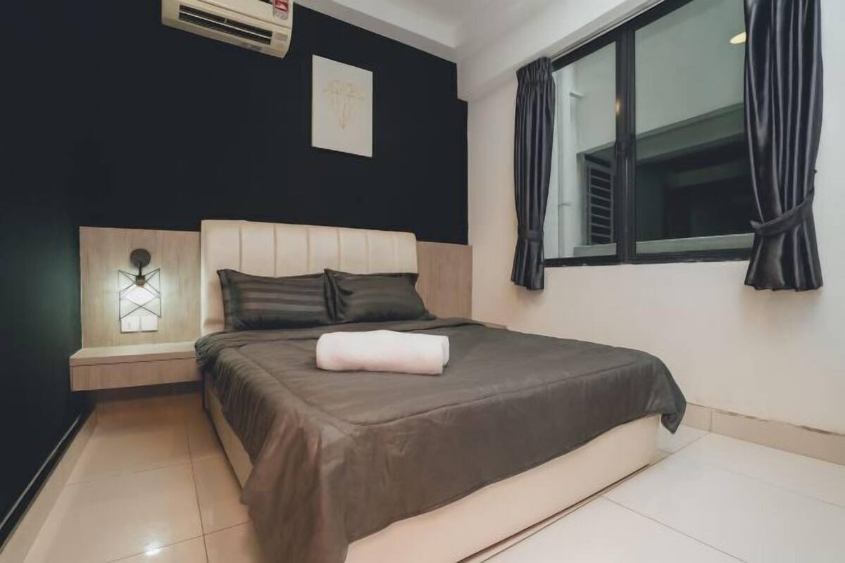 A bedroom with a bed, a nightstand, a wall-mounted air conditioner, a window with curtains, and a wall art piece.