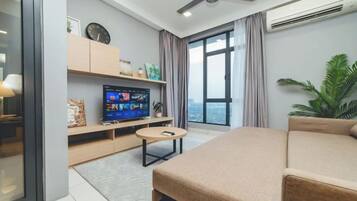 Una sala moderna con un televisor de pantalla plana, un sofá, una mesa de centro y un gran ventanal con cortinas.