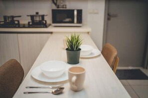 Une table à manger avec des assiettes, une tasse et des couverts, une plante en pot et un four à micro-ondes en arrière-plan.