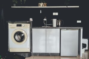 Une cuisine compacte équipée d’un lave-linge, d’un réfrigérateur et d’un plan de travail sur lequel se trouve une machine à café.