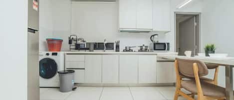 A compact kitchen with a washing machine, microwave, and a dining area with a chair.
