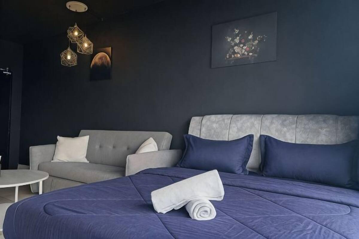 A modern hotel room with a large bed, a grey sofa, and a small round table.