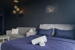 Une chambre d’hôtel moderne avec un grand lit, un canapé gris et une petite table ronde.