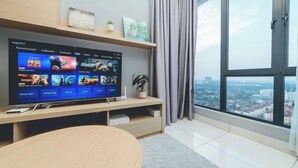 Una sala de estar moderna con un televisor de pantalla plana grande sobre un soporte de madera, una mesa redonda de madera y vistas a la ciudad a través de amplias ventanas.