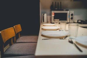 A dining table set with plates, cutlery, and glasses, with a microwave in the background. - 1Tebrau Laconic Lux Suite 1BR nr Columbia (Johor Bahru)