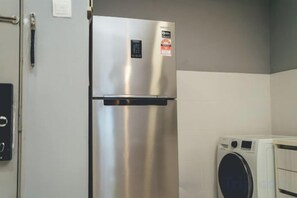 A stainless steel refrigerator with a digital control panel, a washing machine, and a door with a handle. - 1Tebrau Laconic Lux Suite 1BR nr Columbia (Johor Bahru)