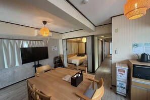 Een kamer met een houten eettafel, stoelen, een flatscreen televisie, een bed, een kitchenette en een badkamer.