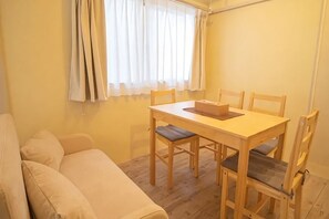 Een kamer met een houten tafel en stoelen, een beige bank en een raam met gordijnen.