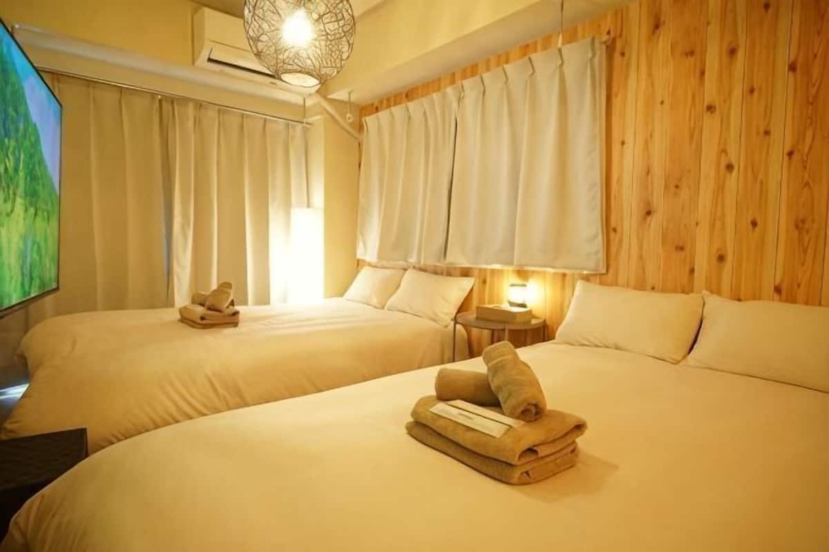 A hotel room with two beds, a TV, a wooden wall, and a window with curtains.