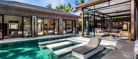 A modern resort with a swimming pool, sun loungers, and a glass-enclosed living area.