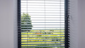 A window with horizontal blinds, a view of greenery and a tree outside. - Charming Holiday Home in Kiel-Windeweer (Kiel-Windeweer)
