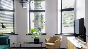 A modern living room with a green sofa, a beige armchair, a coffee table with vases, a potted plant, and a TV on a wooden cabinet. - Charming Holiday Home in Kiel-Windeweer (Kiel-Windeweer)