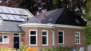A brick house with solar panels on the roof, a garden with plants and flowers, and two Adirondack chairs. - Charming Holiday Home in Kiel-Windeweer (Kiel-Windeweer)