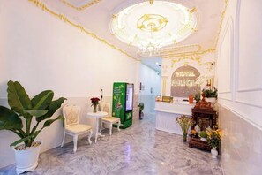Eine Hotelhalle mit Marmorboden, einer Rezeption, einer grünen Verkaufsmaschine und einer Chandelüstere.