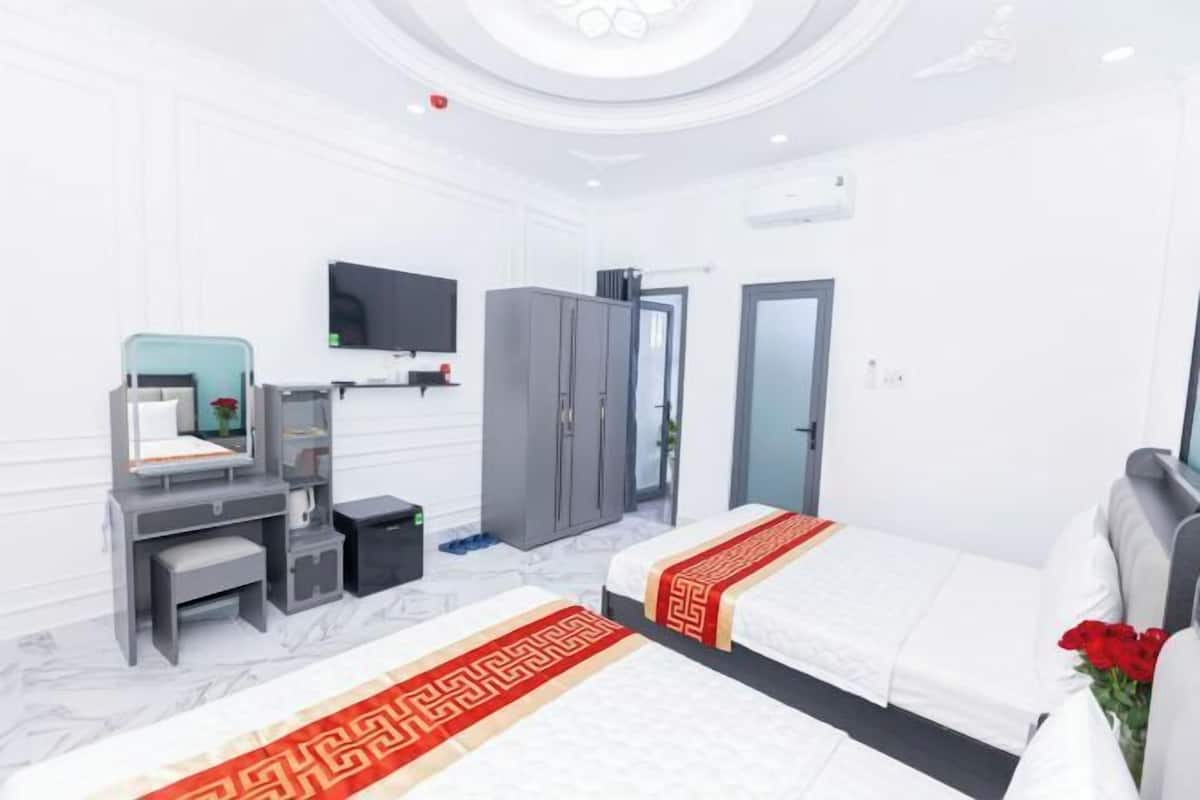 Quarto de hotel com duas camas, uma escrivaninha, televisão e um guarda-roupa.