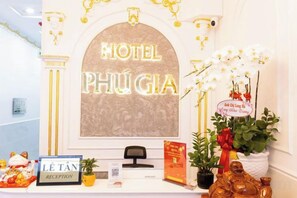 A reception desk at HOTEL PHÚGIA with a sign indicating the reception area, a computer, a small potted plant, and a decorative item. - Phu Gia Hotel 2160 Huynh Tan Phat (Ho Chi Minh City)