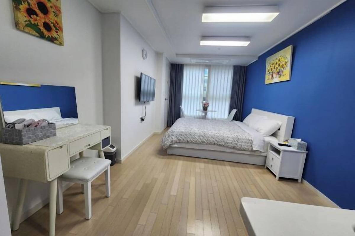 A hotel room with a bed, a desk, a chair, a TV, and a window with curtains.