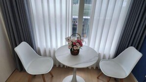A room with a round table, two white chairs, a vase with flowers, and a view through sheer curtains. - Haeundae Bada Stay (Busan)