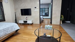 A modern hotel room with a bed, a TV, a small white cabinet, a glass coffee table, and a view of the hallway. - Haeundae Bada Stay (Busan)