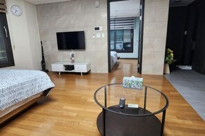 A modern hotel room with a bed, a TV, a small white cabinet, a glass coffee table, and a view of the hallway. - Haeundae Bada Stay (Busan)