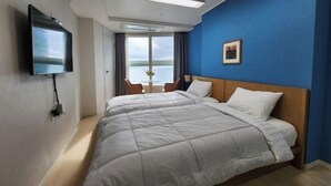 A hotel room with a bed, a TV, a window with a view, and a small table. - Haeundae Bada Stay (Busan)