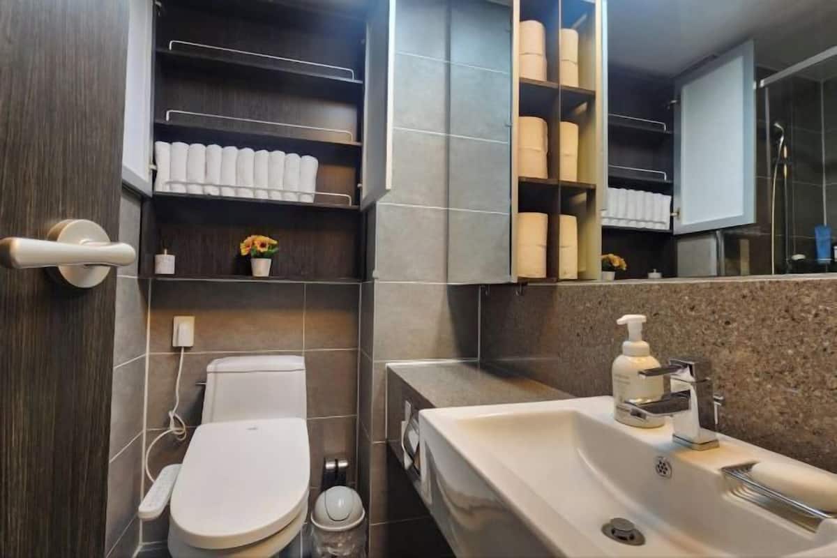 A modern bathroom with a toilet, sink, and shelves with toiletries.
