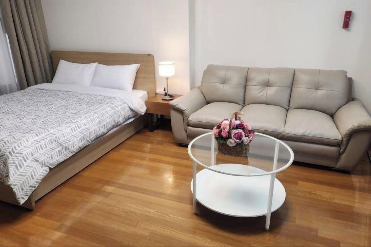 Une chambre d’hôtel avec un lit, un canapé, une table basse ronde en verre et une table de chevet avec une lampe.