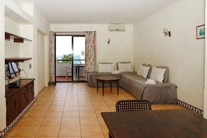 A room with a sofa, a dining table, a TV, and a balcony with curtains.