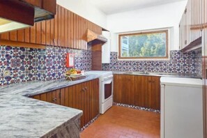 Eine Küche mit Holzausstattung, einer gefliesten Spritzschutzwand, einem Fenster und einer Marmorarbeitsplatte.