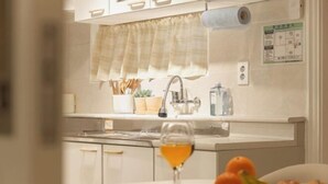 Una cucina con un piano di lavoro bianco, un lavandino, una finestra con tenda e un bicchiere di succo d'arancia sul tavolo.