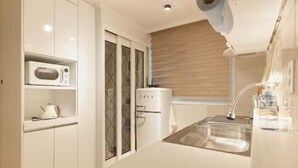 Una cucina compatta con mobili bianchi, un forno a microonde, un erogatore d'acqua e un lavandino.