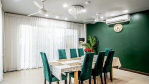 A dining area with a table set for six, green upholstered chairs, a chandelier, and a clock on the wall. - The Ace 6 Bedrooms 6 Bathrooms Villa With Free Bills (Pattaya)