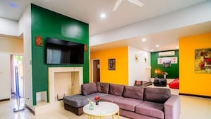 A modern living room with a sectional sofa, a round coffee table, and a flat-screen TV mounted on a green wall. - The Ace 6 Bedrooms 6 Bathrooms Villa With Free Bills (Pattaya)