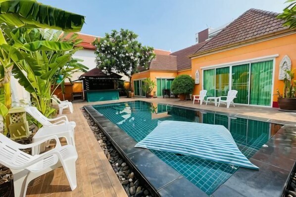 A swimming pool with lounge chairs, a covered seating area, and a house with a tiled roof and green shutters. - The Ace 6 Bedrooms 6 Bathrooms Villa With Free Bills (Pattaya)