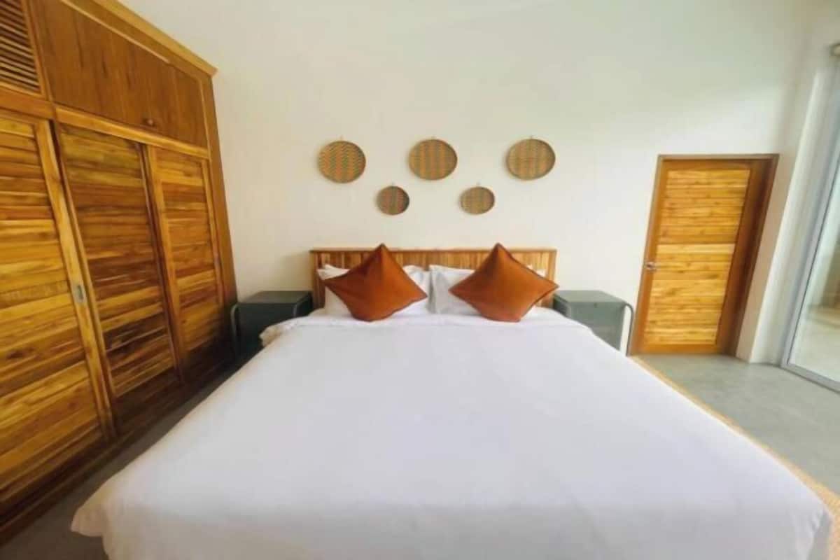 A bedroom with a large wooden wardrobe, a bed with white bedding, two brown pillows, and a wall with circular decorations.