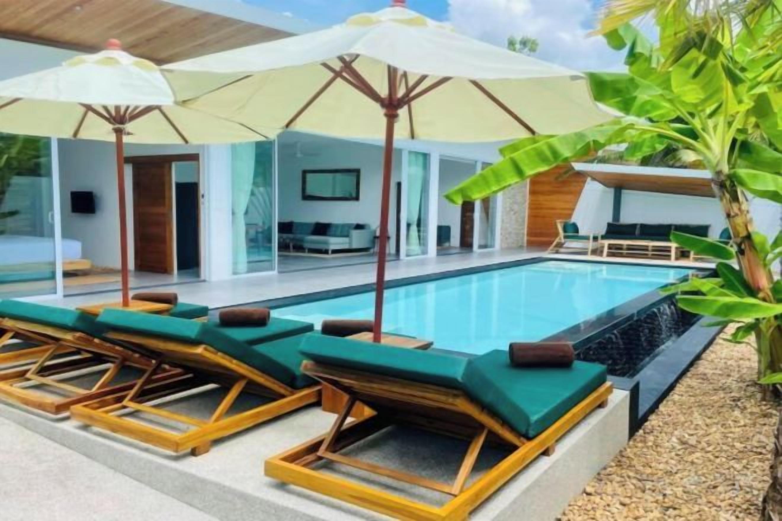A pool area with lounge chairs and umbrellas, a modern building with a flat roof, and a large window.