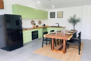 A compact kitchen with a black refrigerator, green cabinets, and a dining table with chairs. - Villa Kurma, 2 bedrooms (Koh Samui)