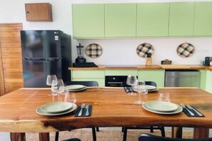 A dining area with a wooden table set for four, a black refrigerator, and light green cabinets in the background. - Villa Kurma, 2 bedrooms (Koh Samui)