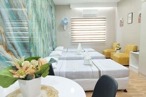 Habitación de hotel con dos camas, una mesita con un florero, un ventilador y una ventana con persianas.