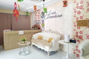 Un espace d’accueil comprenant un comptoir de réception, un canapé blanc, une petite table ronde et un mur recouvert d’un papier peint à motifs floraux.
