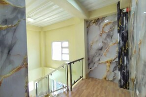 Interior de hotel com parede de mármore, piso de madeira e guarda-corrimão de vidro.