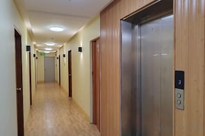 Pasillo de hotel con puertas de madera, un ascensor y suelo de baldosas.
