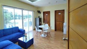Um quarto com sofá azul, mesa de centro, mesa de jantar com cadeiras e uma janela grande.