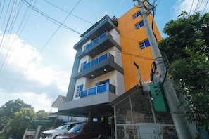 Un edificio de varios pisos con balcones, una entrada con portón y una línea eléctrica visible.