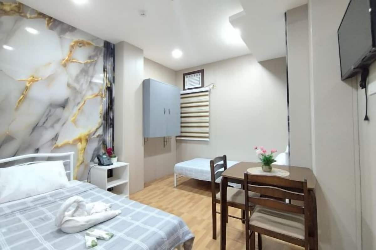 Una habitación de hotel con cama, escritorio, silla, televisor, armario y pared de mármol.